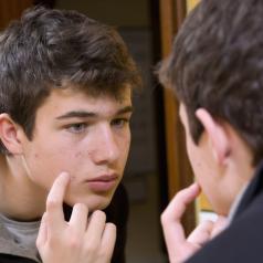 Teenager examining acne in the mirror