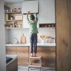 Young boy standing on step stool to steal cookies form kitchen cupboard