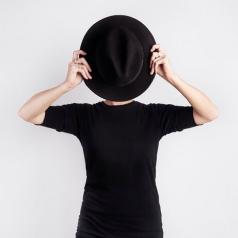 Woman holding up a black hat to hide her face