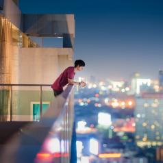 Man in red shirt leans on railing to look at city