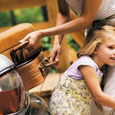 Child hugging parent as they pack suitcases into car for a trip
