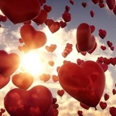 Red heart balloons floating in sky with sun in background.